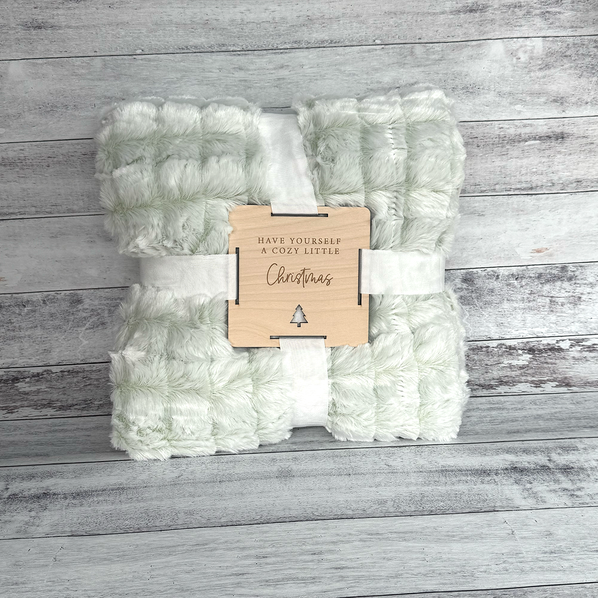 Folded green and white blanket with a wooden tag on a wooden surface