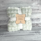 Folded green and white blanket with a wooden tag on a wooden surface