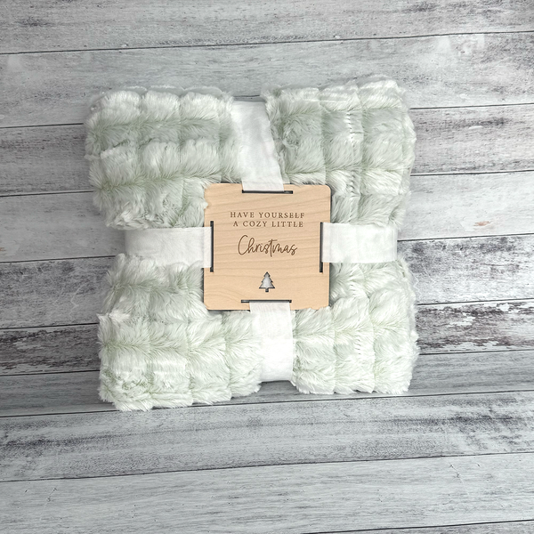 Folded green and white blanket with a wooden tag on a wooden surface