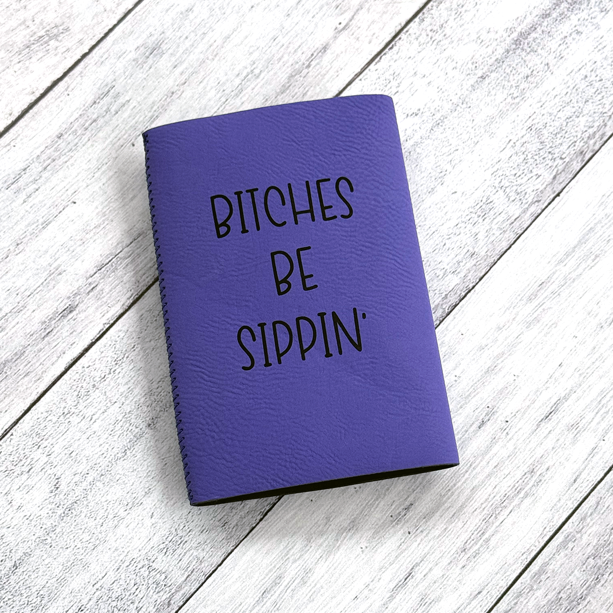 Purple notebook with 'Bitches Be Sippin'' text on a wooden surface