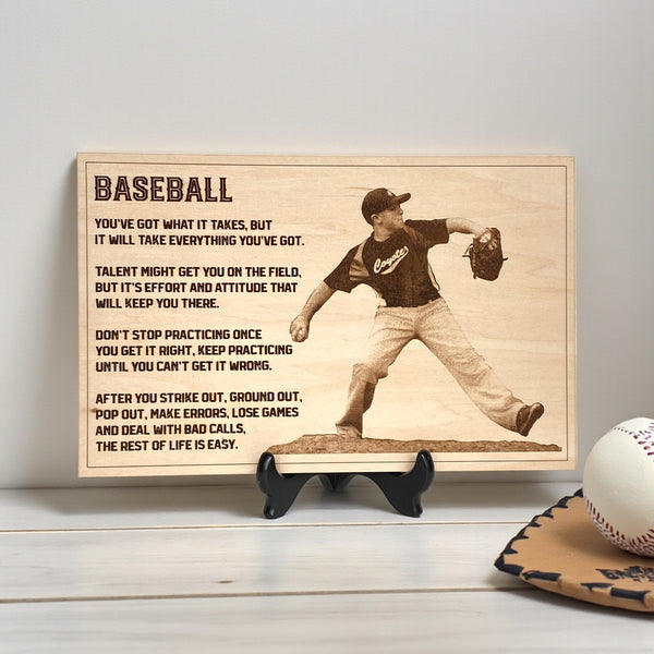 Wooden plaque engraved with baseball player photo and text on a stand, with a baseball and glove on a wooden surface.